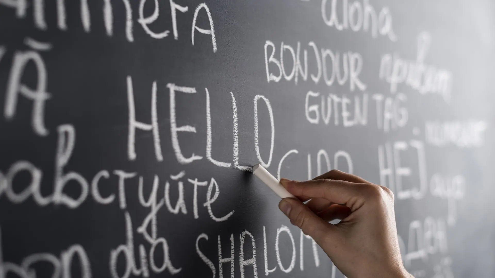 Mano escribiendo con una tiza en una pizarra sobre el idioma más difícil de aprender