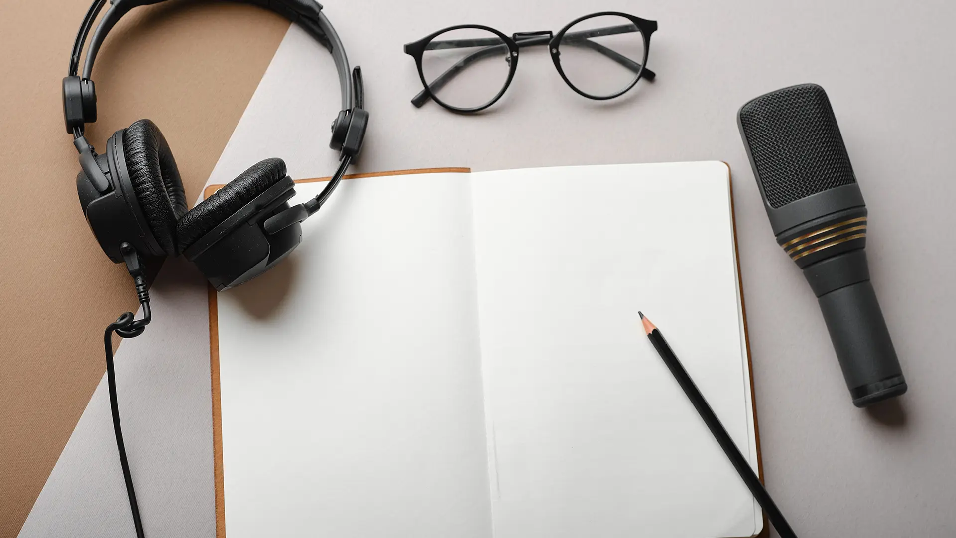 Un escritorio con unos auriculares, unas gafas, un micrófono, un lápiz y una libreta para transcripción automática