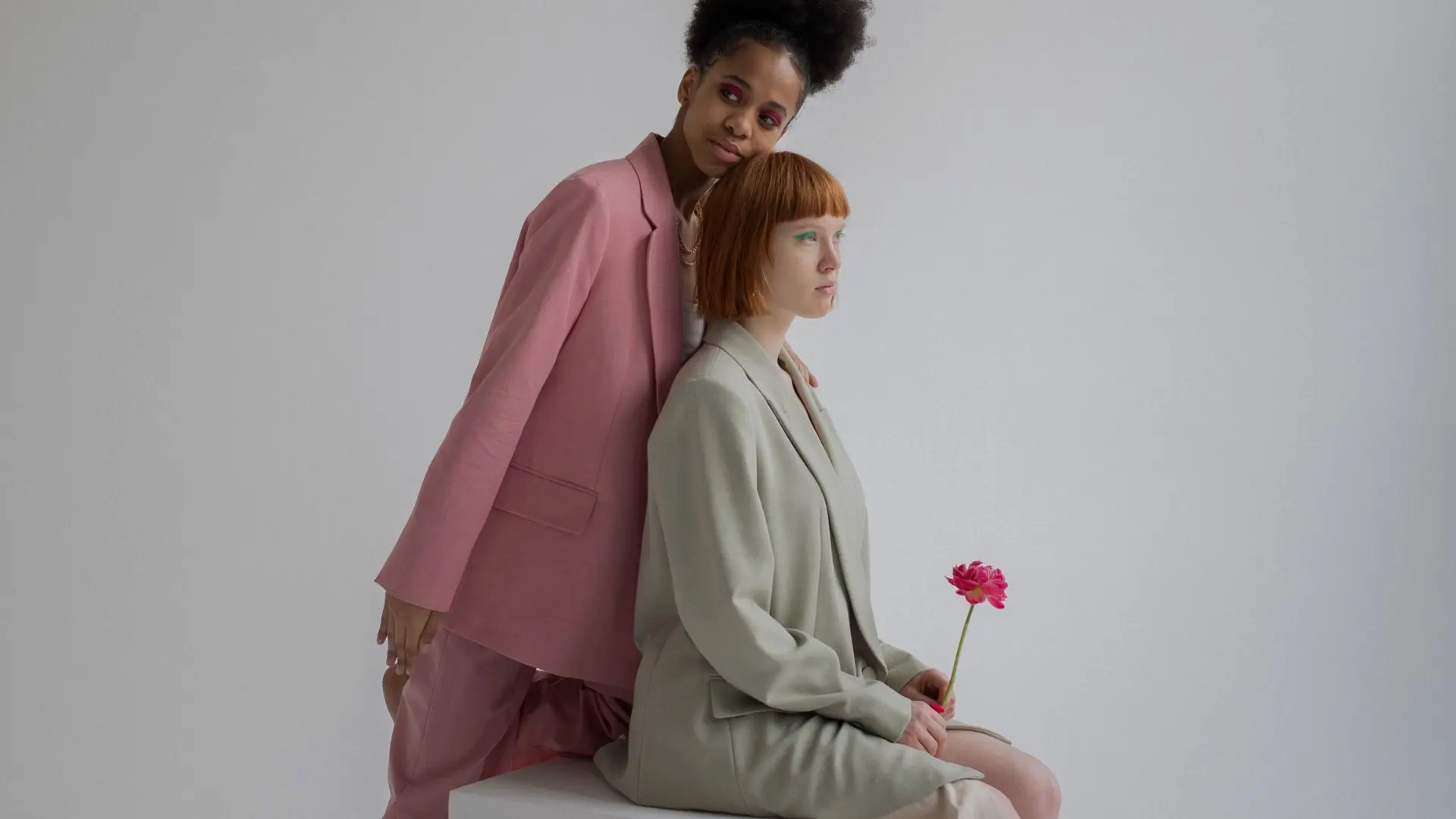 Dos modelos en una sesión de fotos con trajes en color pastel sujetando una flor para servicios de traducción de moda