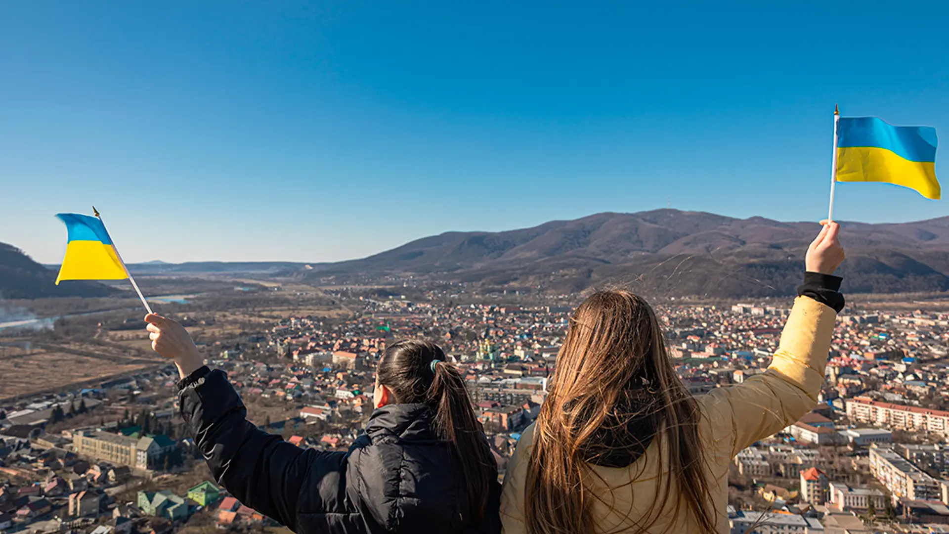Dos mujeres de espaldas sujetan banderas de Ucrania mirando hacia el paisaje de Ucrania representando un traductor ucraniano español