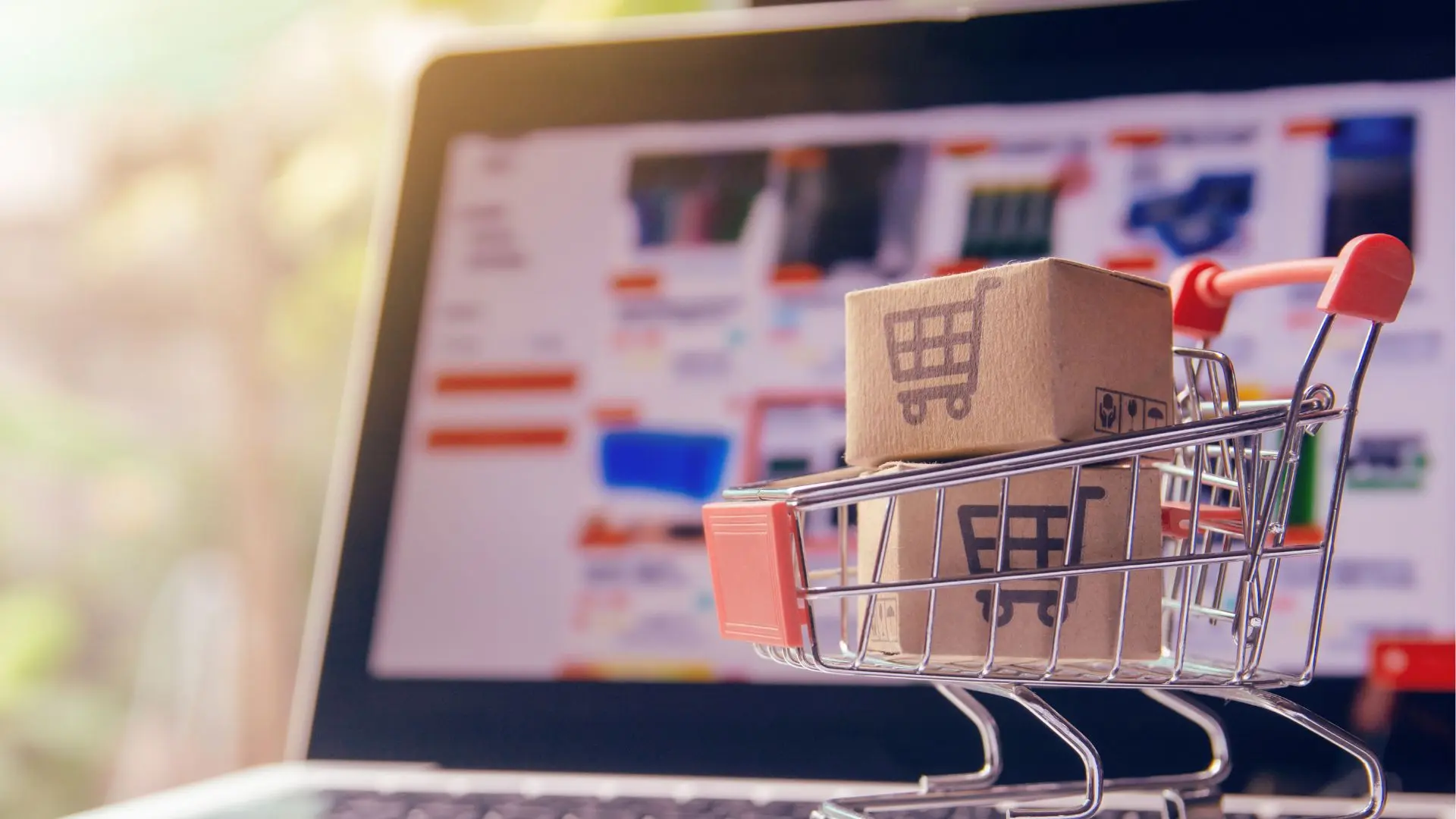 Carrito pequeño de compra con cajas de cartón dentro puesto sobre un portátil con un ecommerce abierto