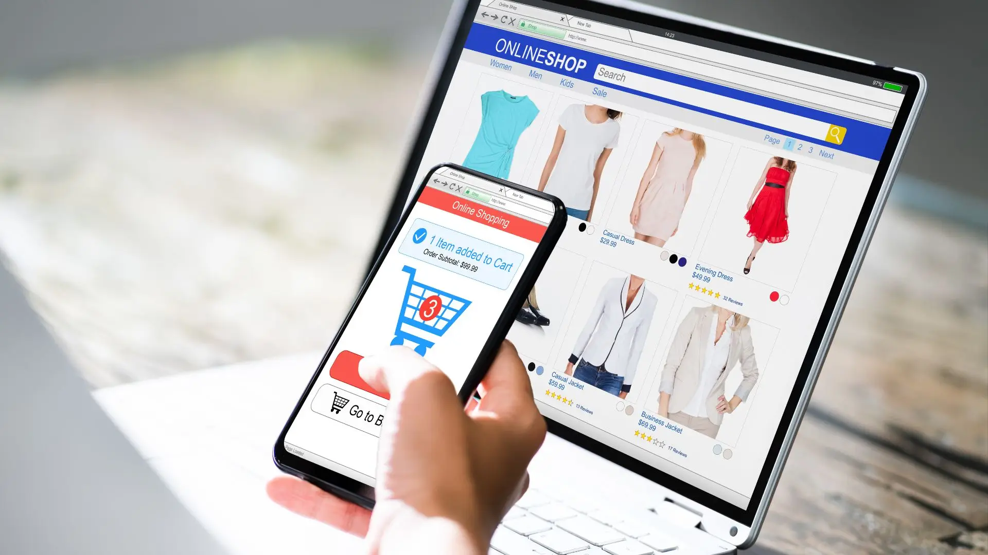 Mano sujetando un teléfono con un carrito de compra en la pantalla y con un ordenador con un ecommerce de ropa abierto
