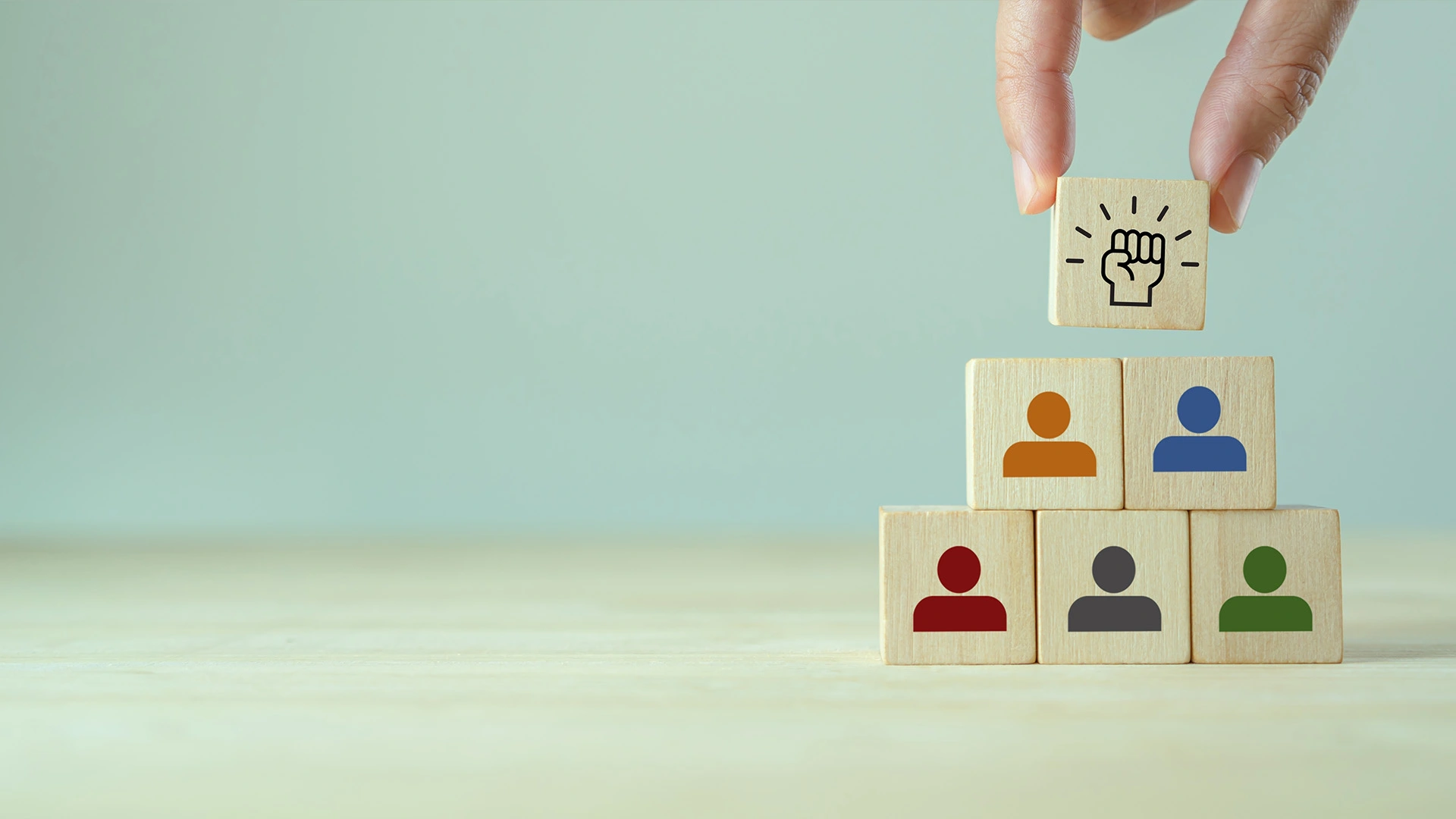 Seis piezas de madera amontonadas, cinco con monigotes de colores y una con un puño para simbolizar equipo