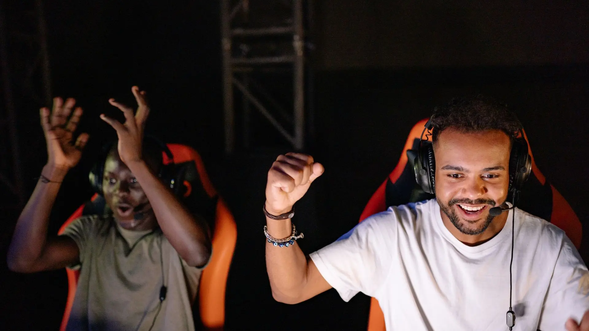 Dos hombres con auriculares con micrófono sentados en sillas gamer celebrando una victoria en localización de videojuegos