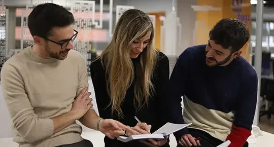 Tres personas del equipo de Linguaserve sentados miran una libreta