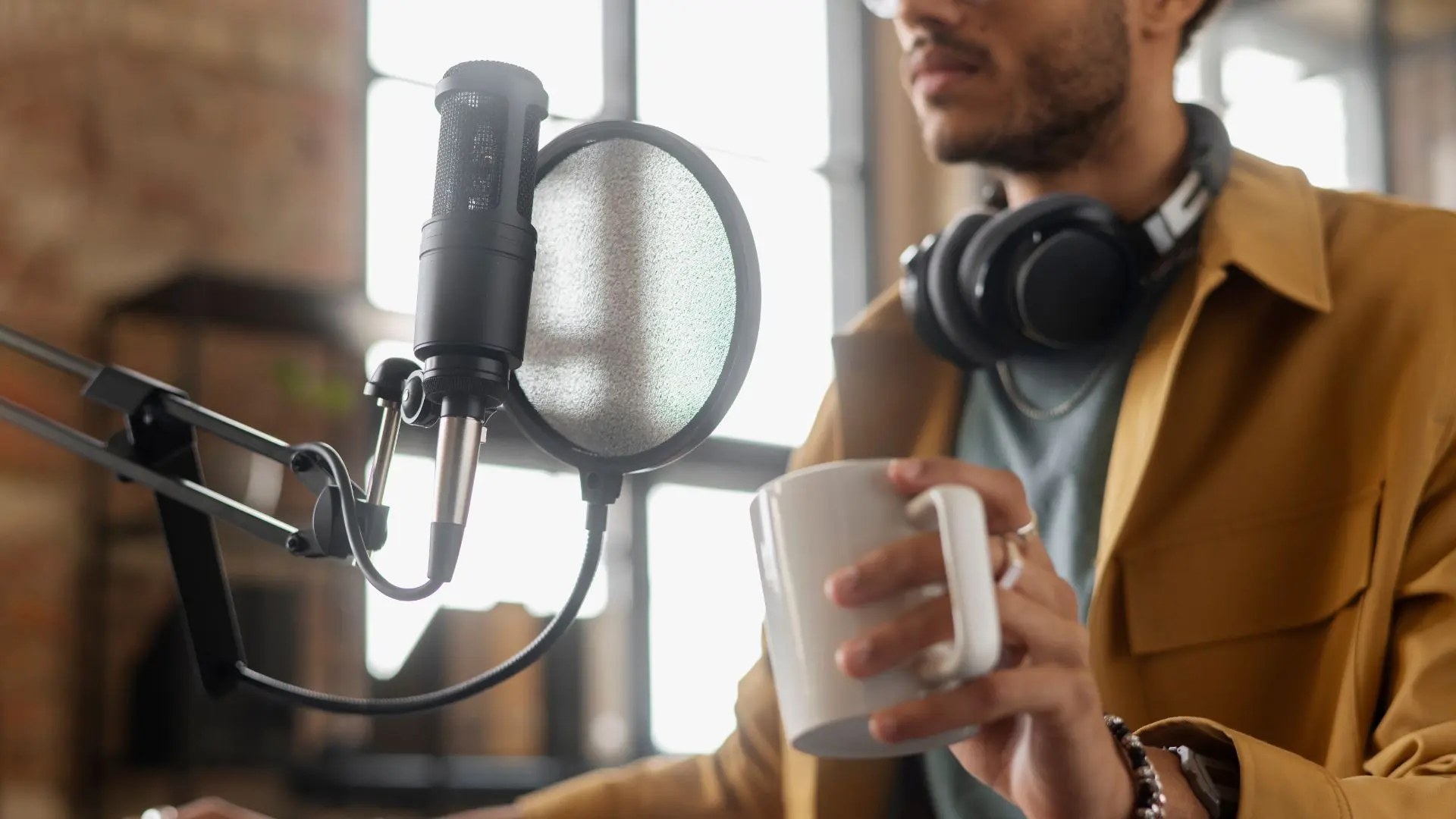Hombre con cascos en el cuello sujeta una taza y habla a un micrófono sobre traducción audiovisual