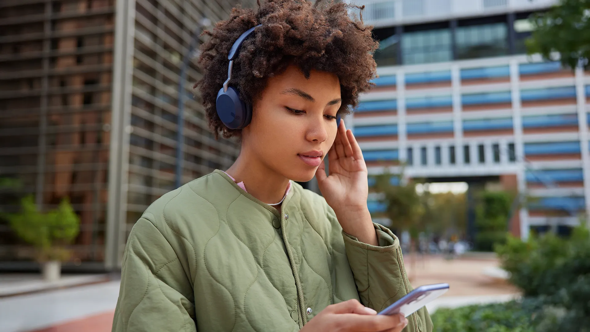 Woman using an AI translator on her phone while using blue headphones and walking in the city
