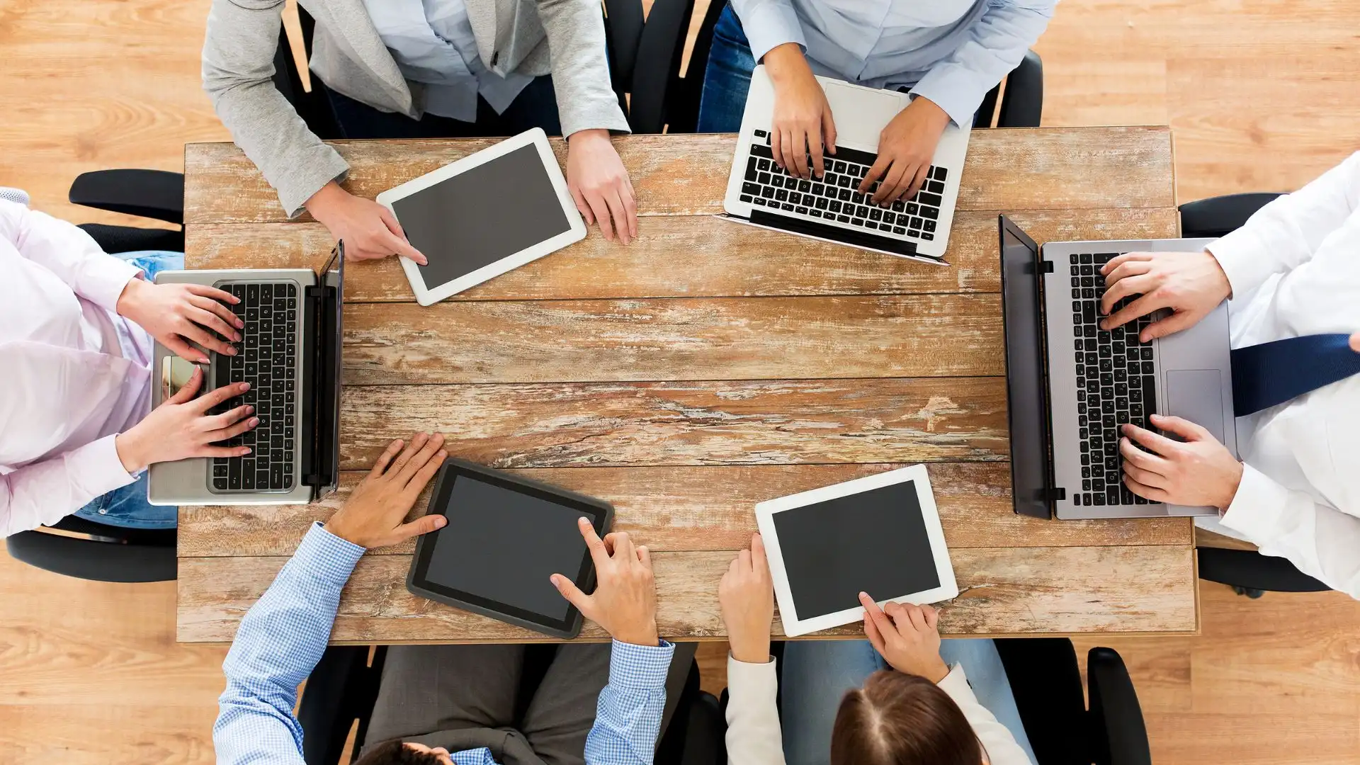 Equipo de personas trabajando en laptops y tablets alrededor de una mesa de madera, representando el valor humano en la traducción web