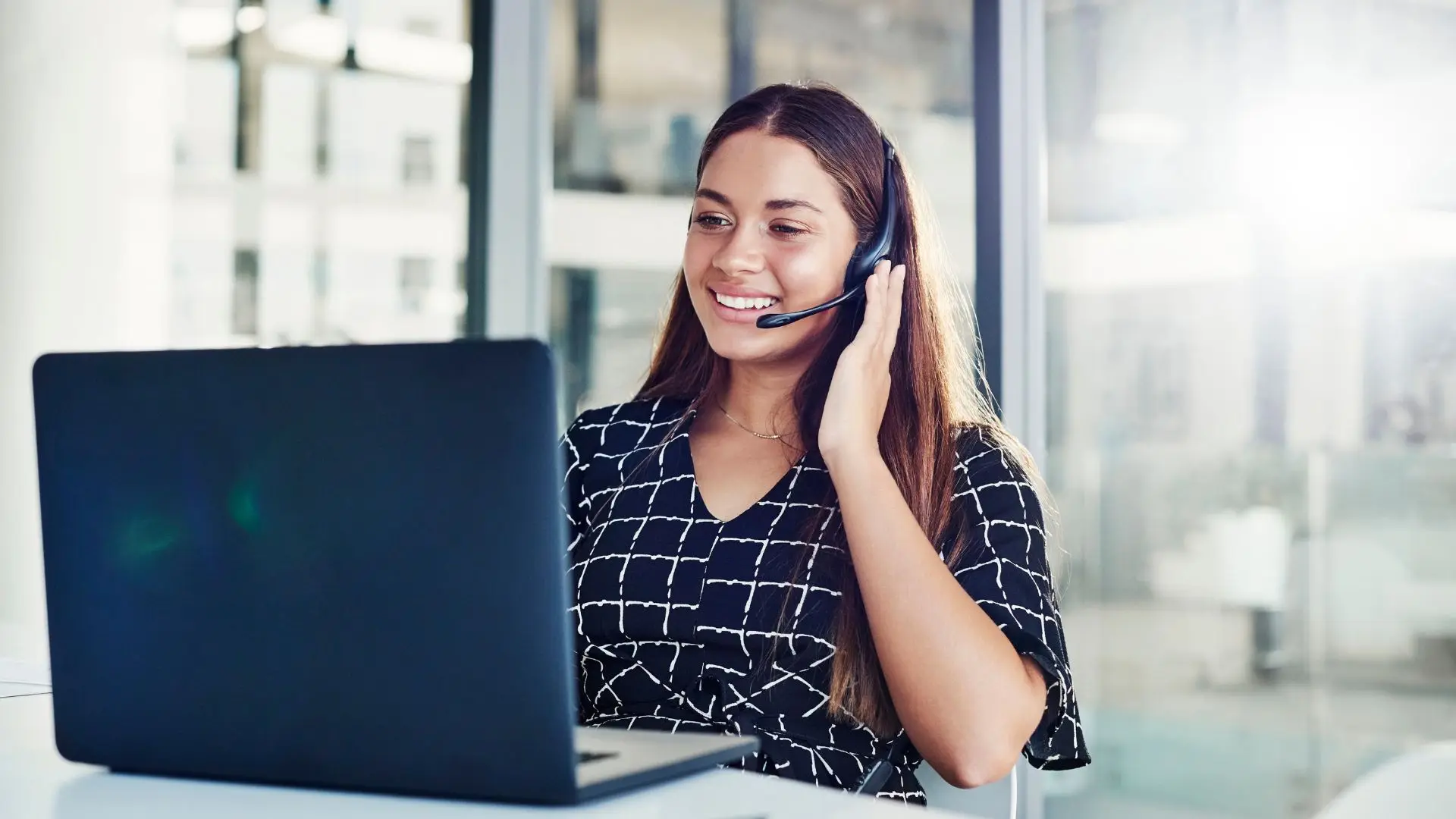 Mujer con auriculares con micrófono sonriendo mirando al ordenador hablando sobre traducción automática neuronal